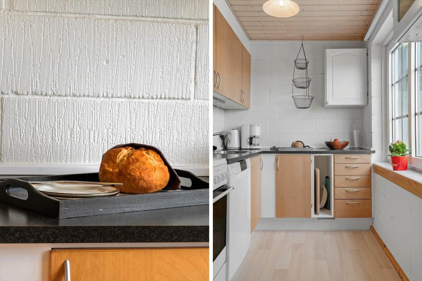 Küche mit Holzschrank und Steinplatten. Brot auf Tablett. Fenster mit Pflanze.