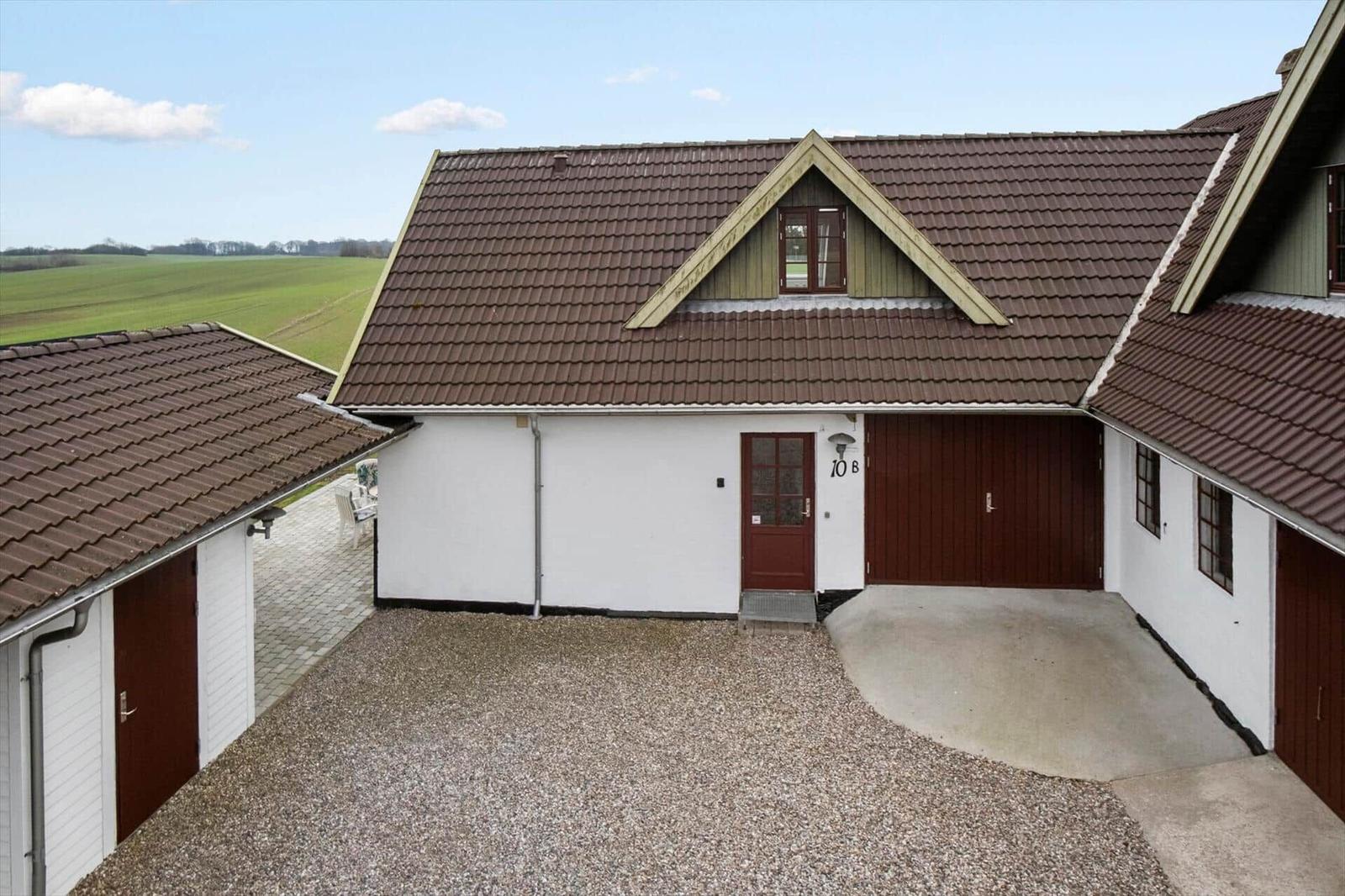 Haus mit braunem Dach, roter Tür und Garage. Grünfelder im Hintergrund.