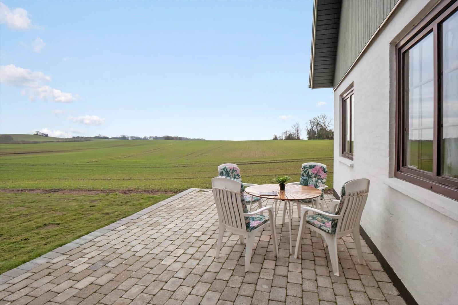 Terrasse mit Tisch und Stühlen, Blick auf grünes Feld.