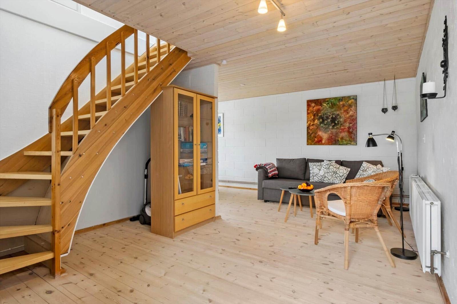 Wohnzimmer mit Holzdecke, Sofa, Stühlen und Treppe.