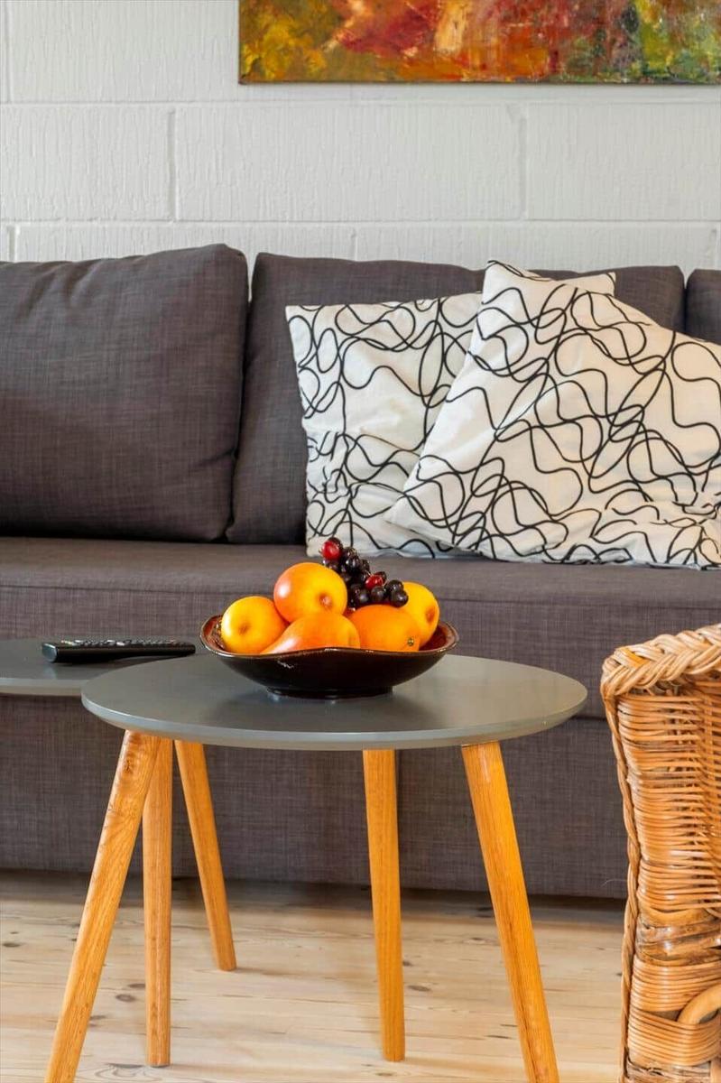 Ein grauer Sofa mit Kissen, ein runder Tisch und Obstschale.