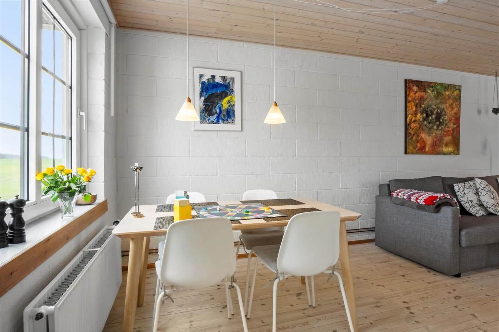 Essbereich mit Tisch, Stühlen und Sofa. Fenster mit Blumen und Wandbilder.