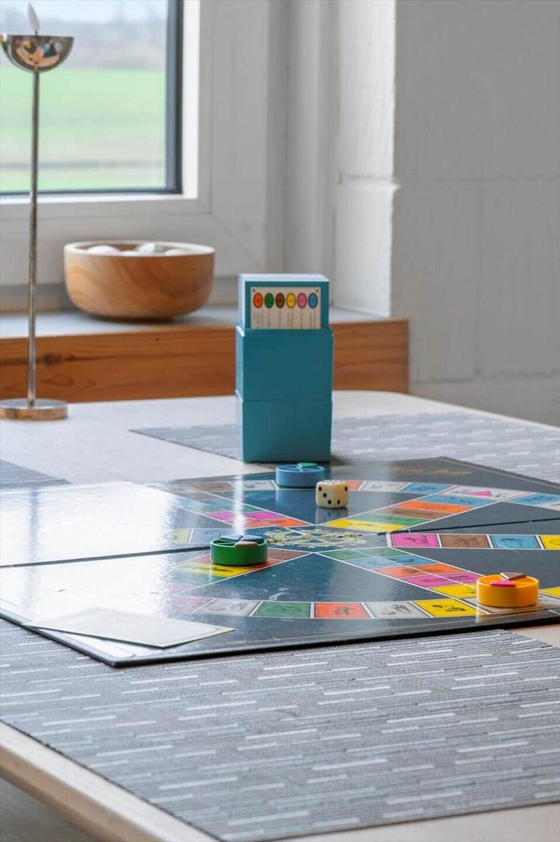 Spielplatte mit Würfeln und Spielsteinen auf Tisch. Fenster mit Blick auf Grünfläche.