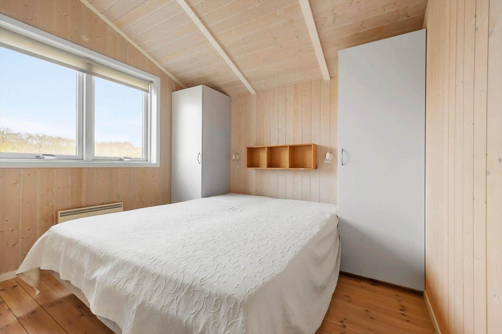 Bedroom with wooden walls, bed, and window. Two wardrobes and wall shelf.