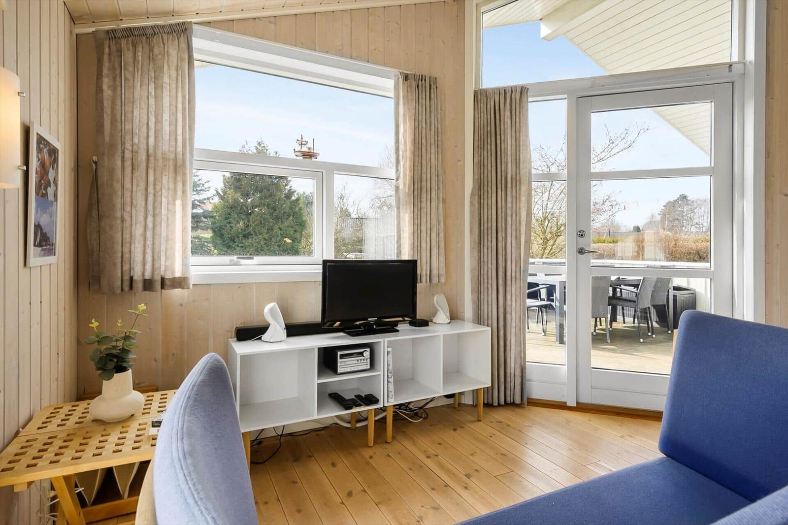 Living room with TV, window, and terrace door. Wooden floor and blue seating.