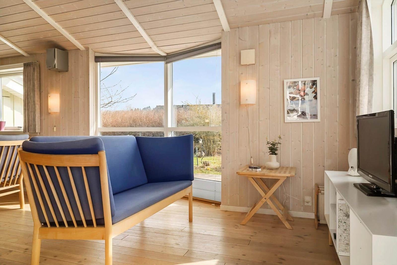 Living room with blue sofa, wooden walls, and large window view.