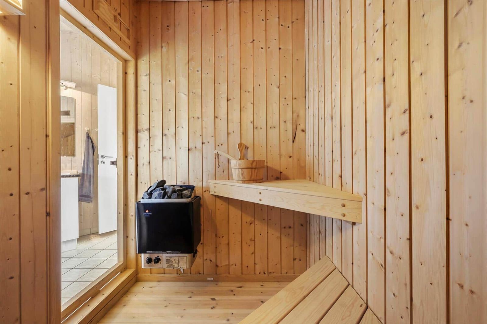 Sauna with wooden walls, bench, and heater. Entrance to bathroom.
