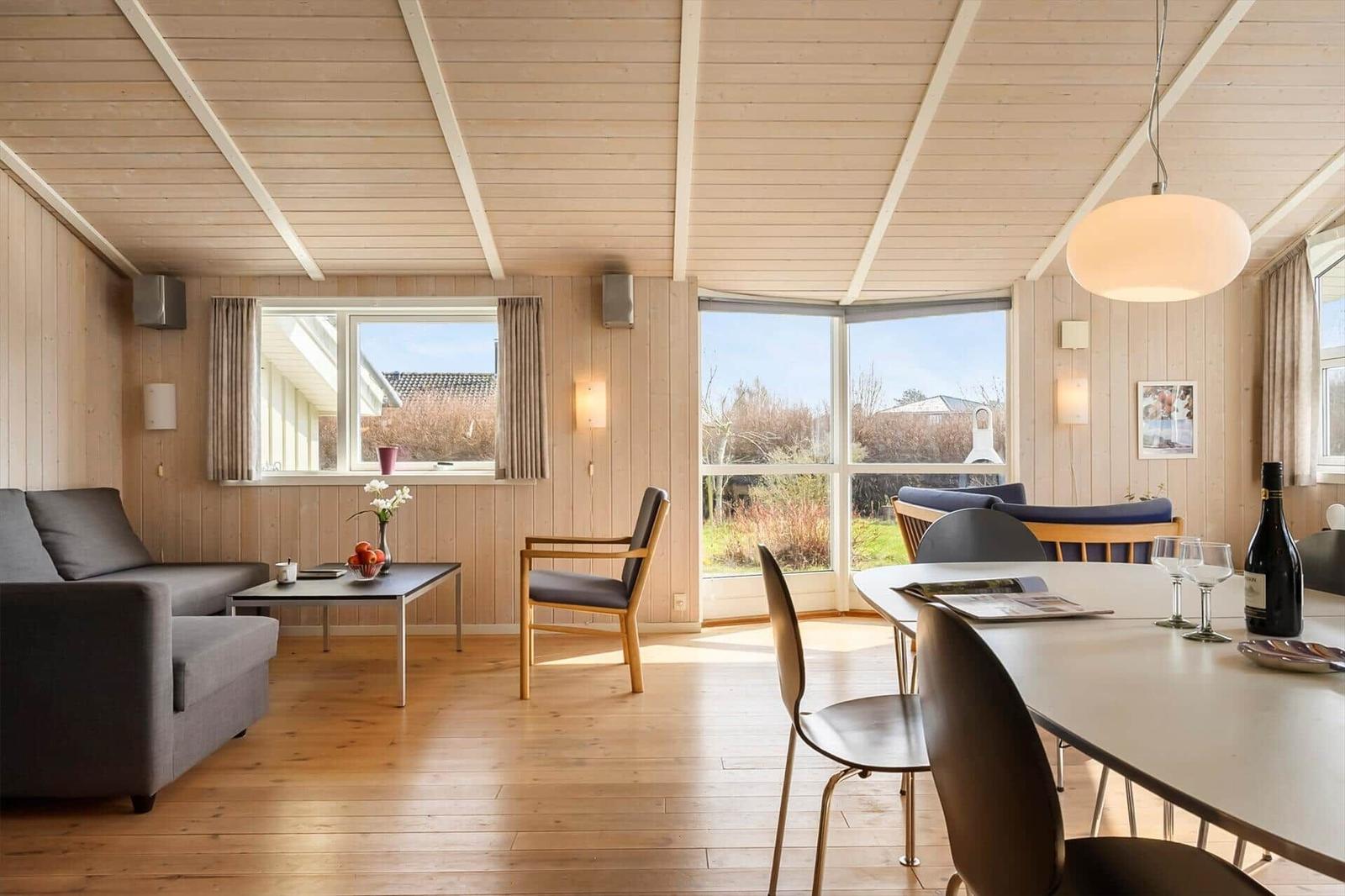 Living and dining area with wooden ceiling, windows, and modern furniture.