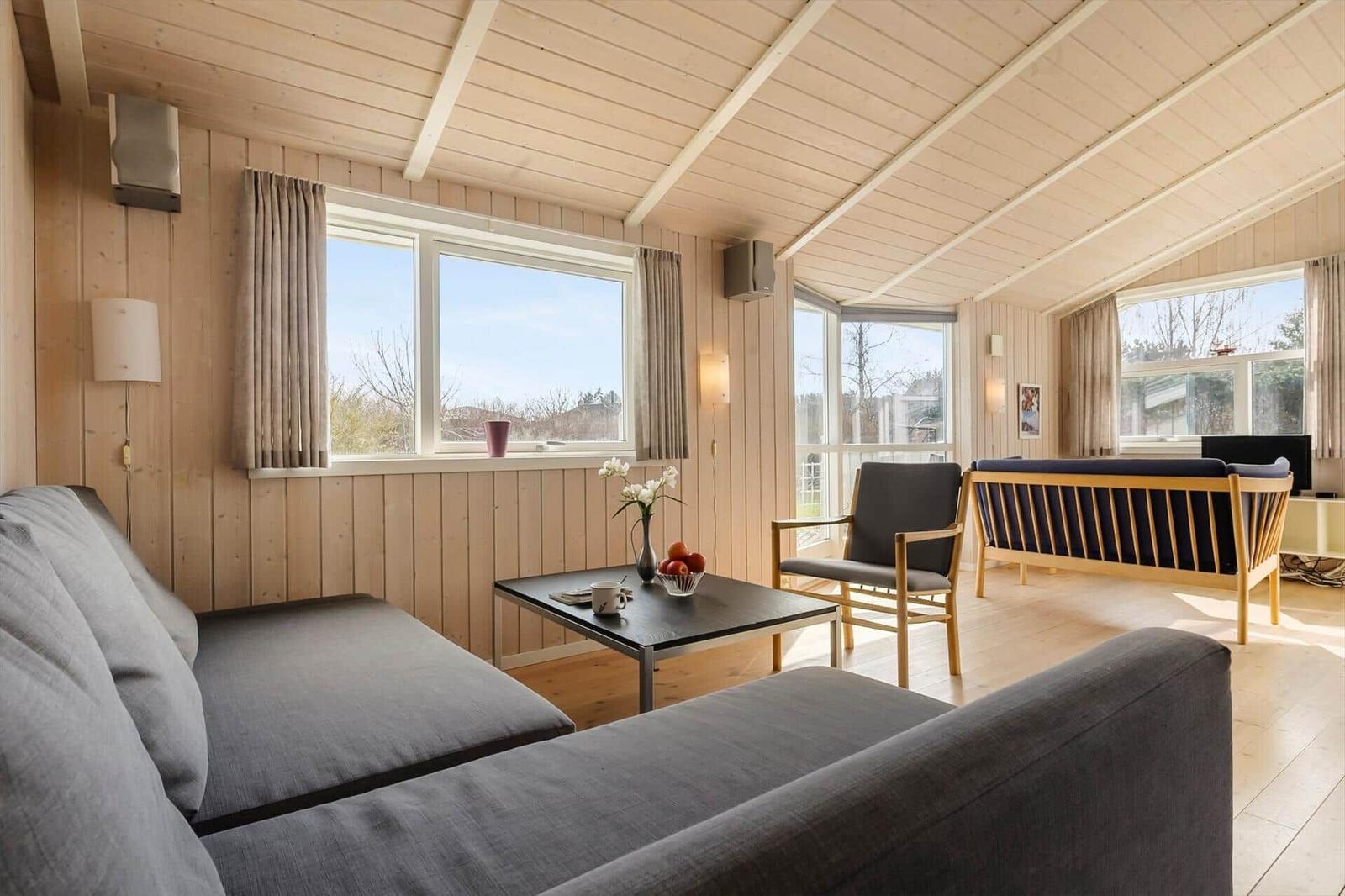 Living room with wooden walls, sofa, chair, and windows.