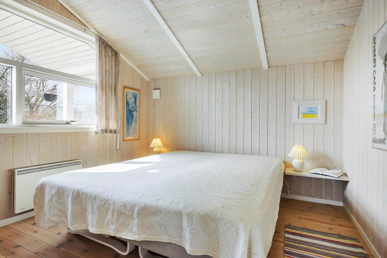 Bedroom with bed, window, and wooden wall. A bedside lamp is next to the bed.