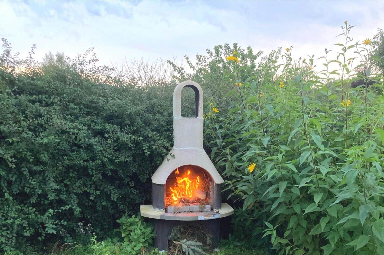 Outdoor stone oven with burning fire in green areas with yellow flowers.