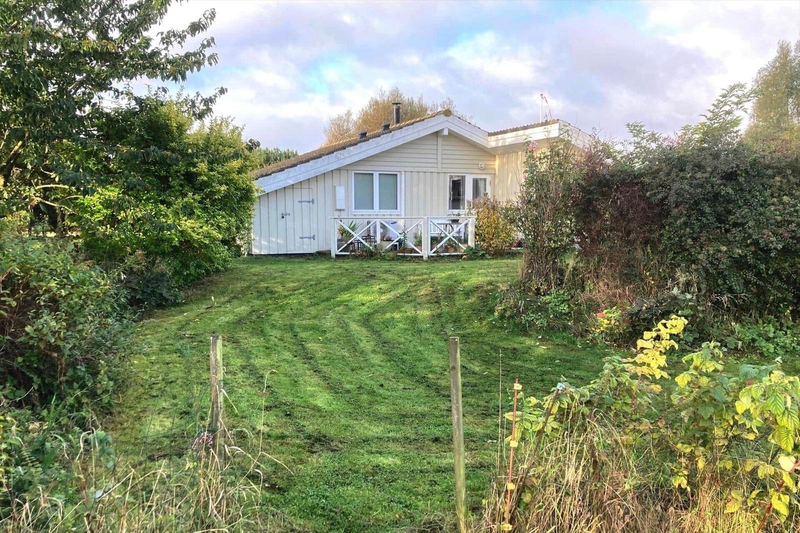 A house with a white fence and green lawn in front of a wooded area.