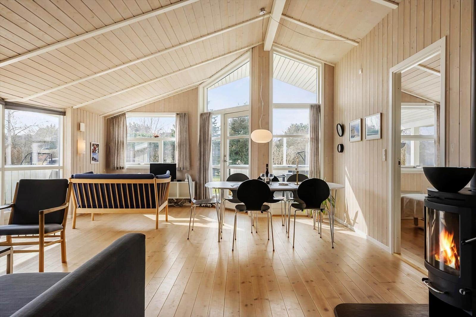 Living room with dining area, wooden floor, and wood-burning stove. Large windows provide ample daylight.