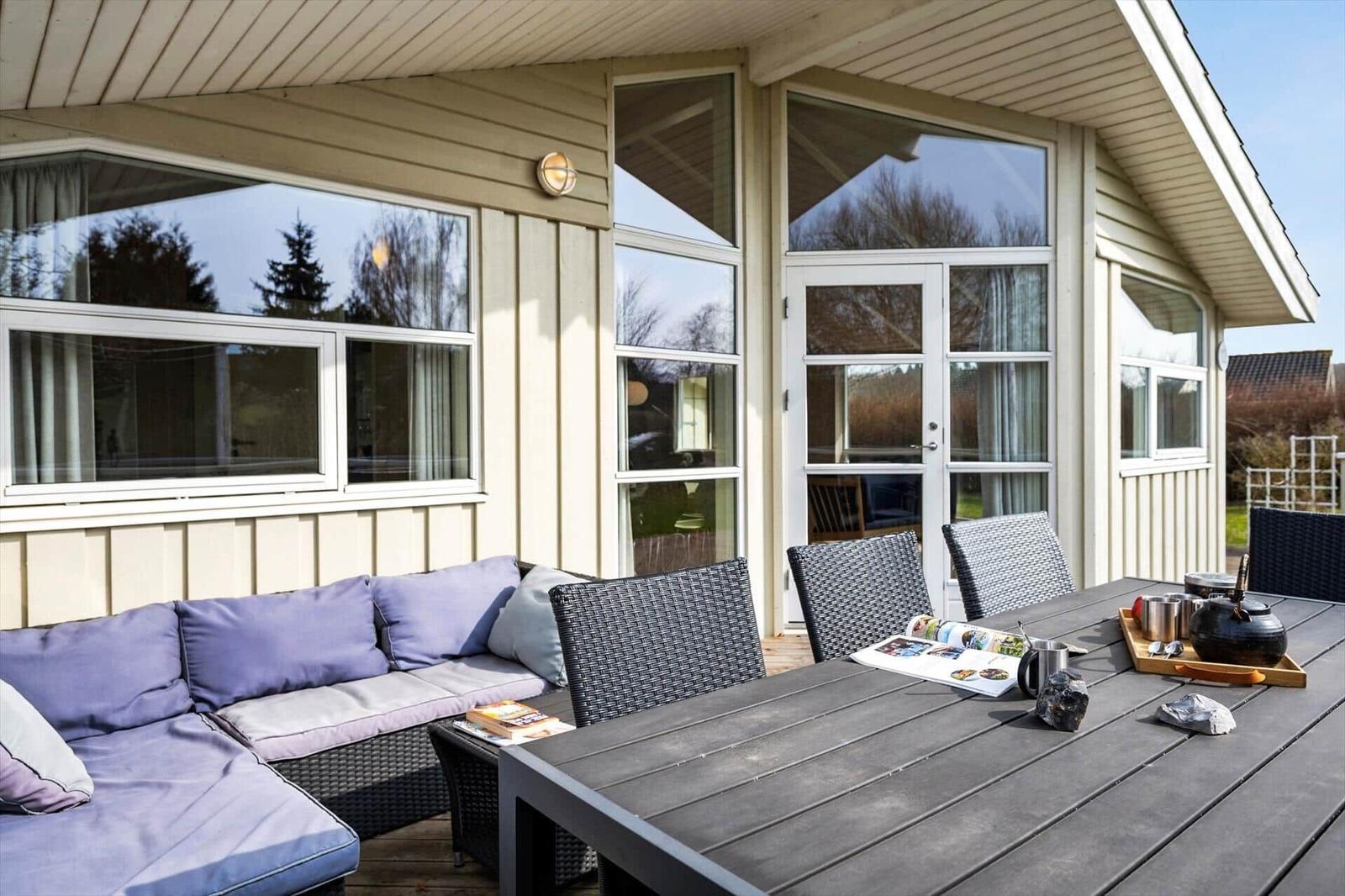 Terrace with seating group and dining table. Glass door and wooden wall visible.