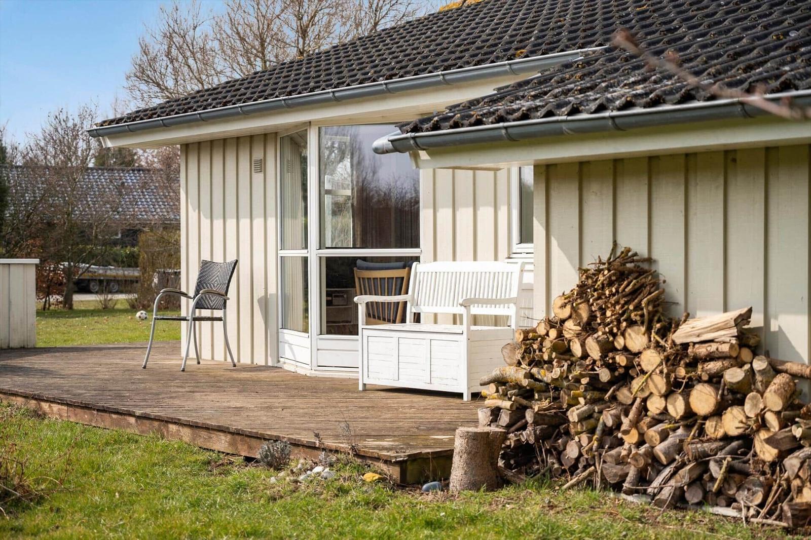 Deck with seating and woodpile in front of a house.