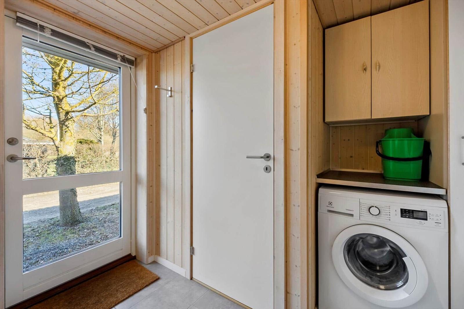 Entrance area with washing machine, wooden walls, and window view of a tree.