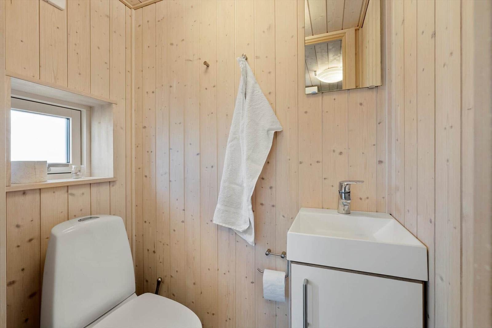Bathroom with toilet, sink, and mirror on wooden wall