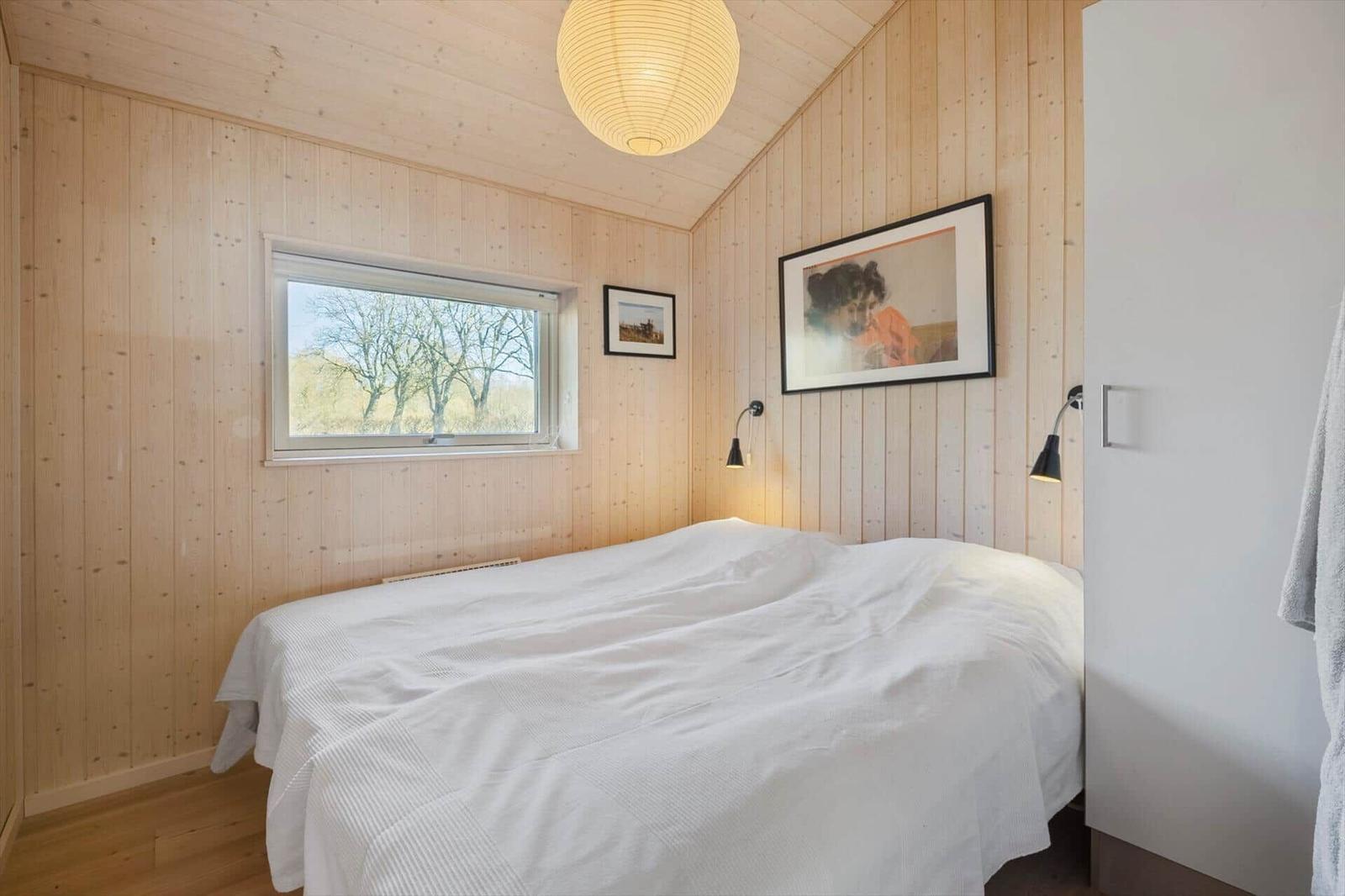 Bedroom with wooden walls, bed, and window overlooking trees.