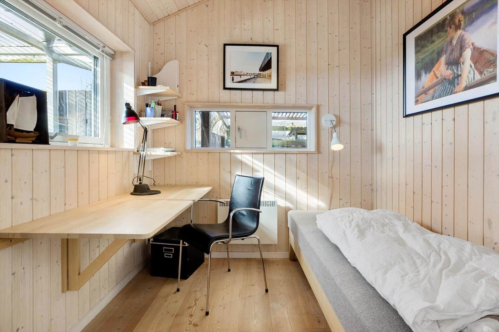 A bedroom with bed, desk, and chair. Wooden walls and windows.