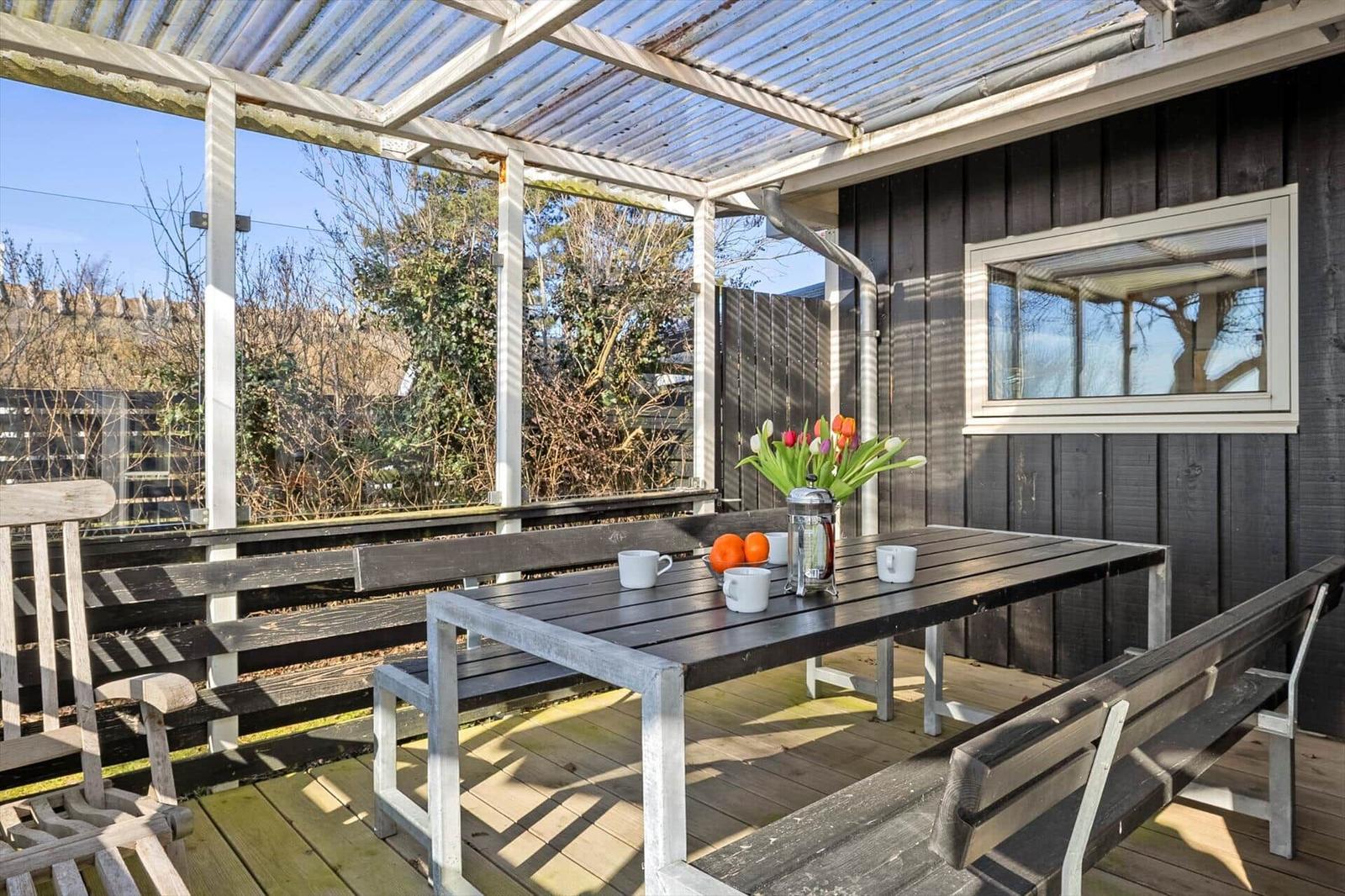 Deck with table, benches, and flowers under a roof.