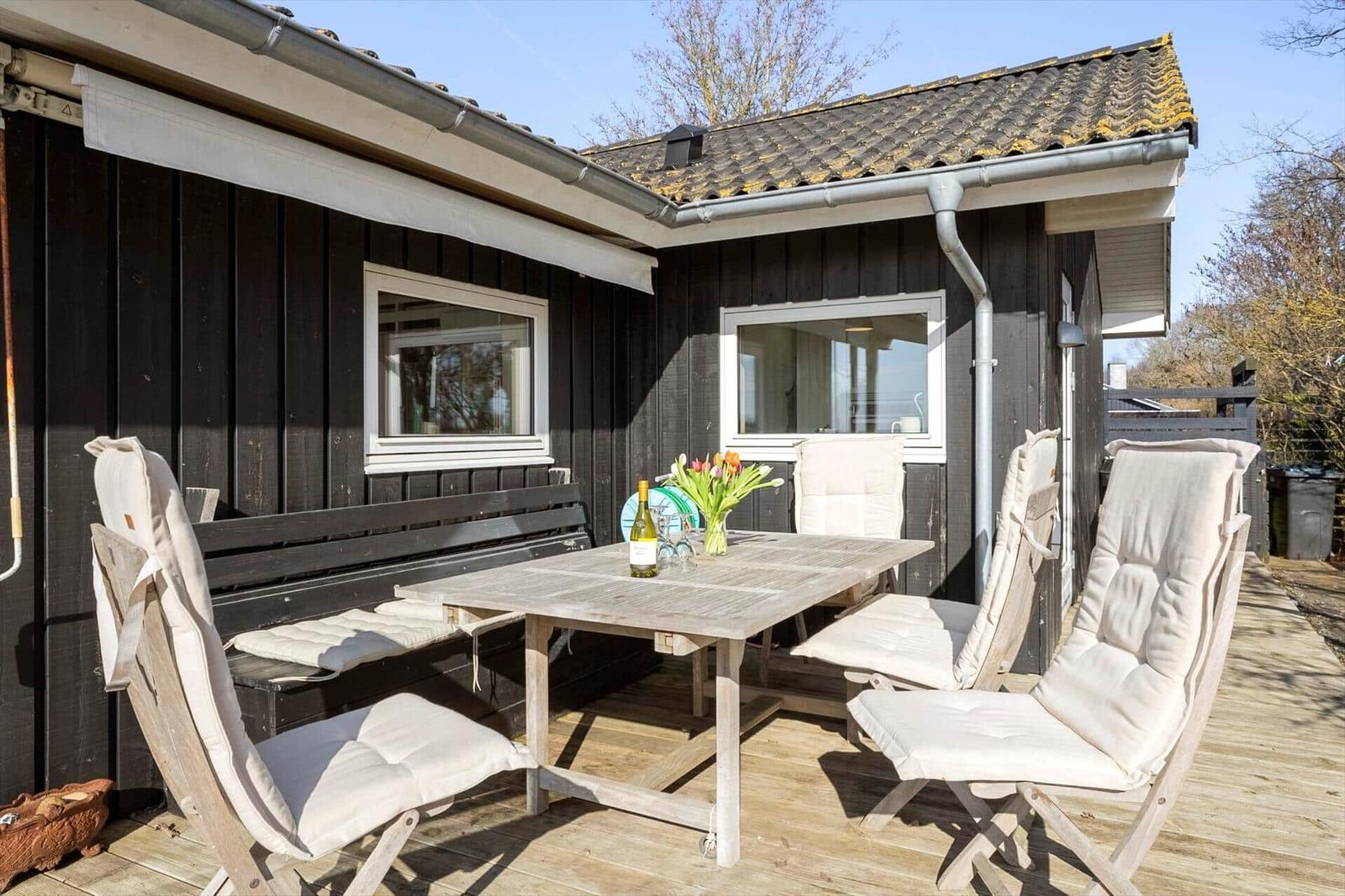 Deck with table, chairs, and flowers in front of a house with dark siding.