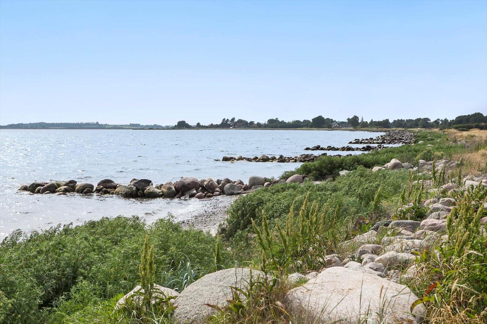 Coast with stones and grass, view of calm water and distant shoreline.