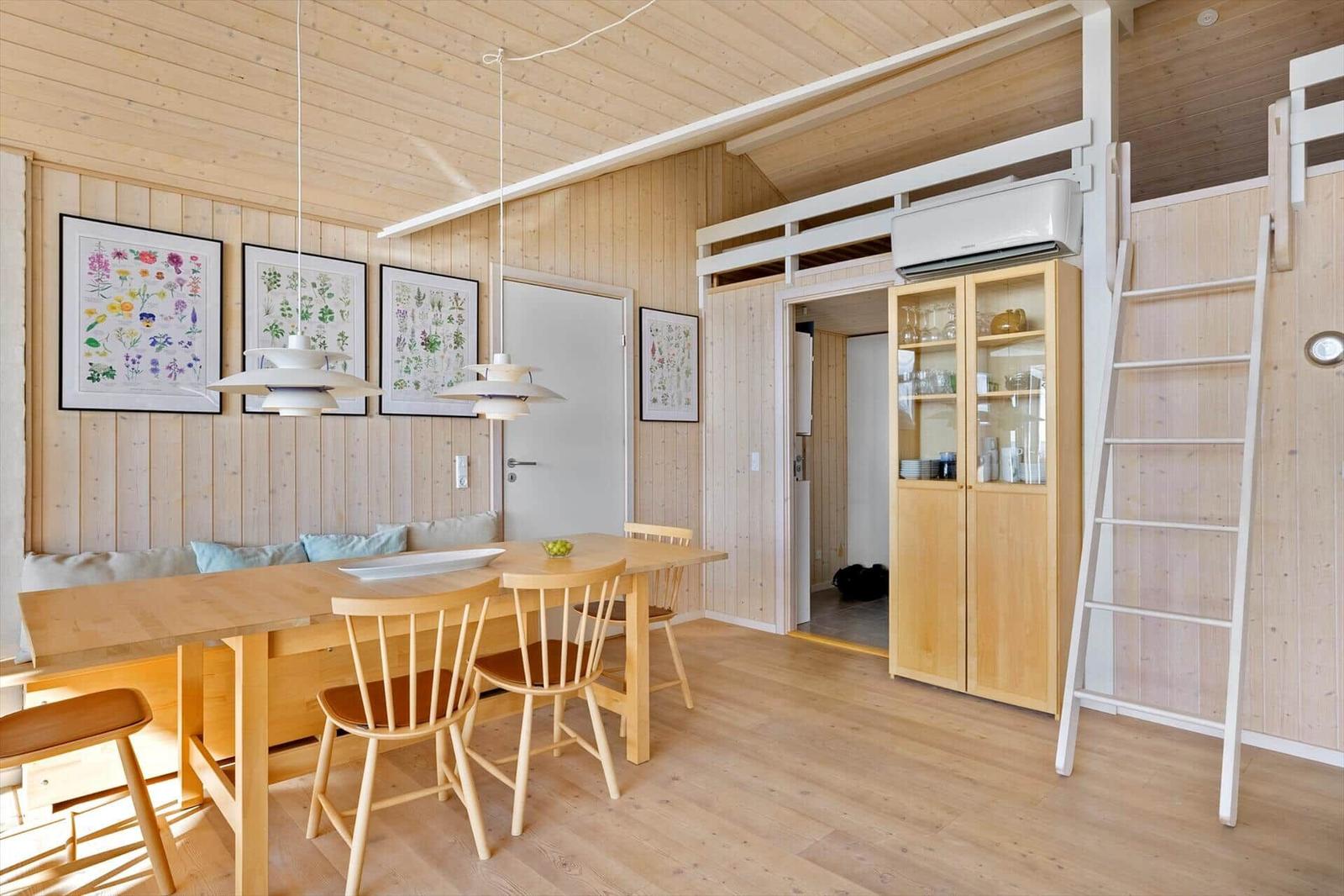 Dining area with wooden table, chairs, and wall art. Upper level with ladder and cabinet.