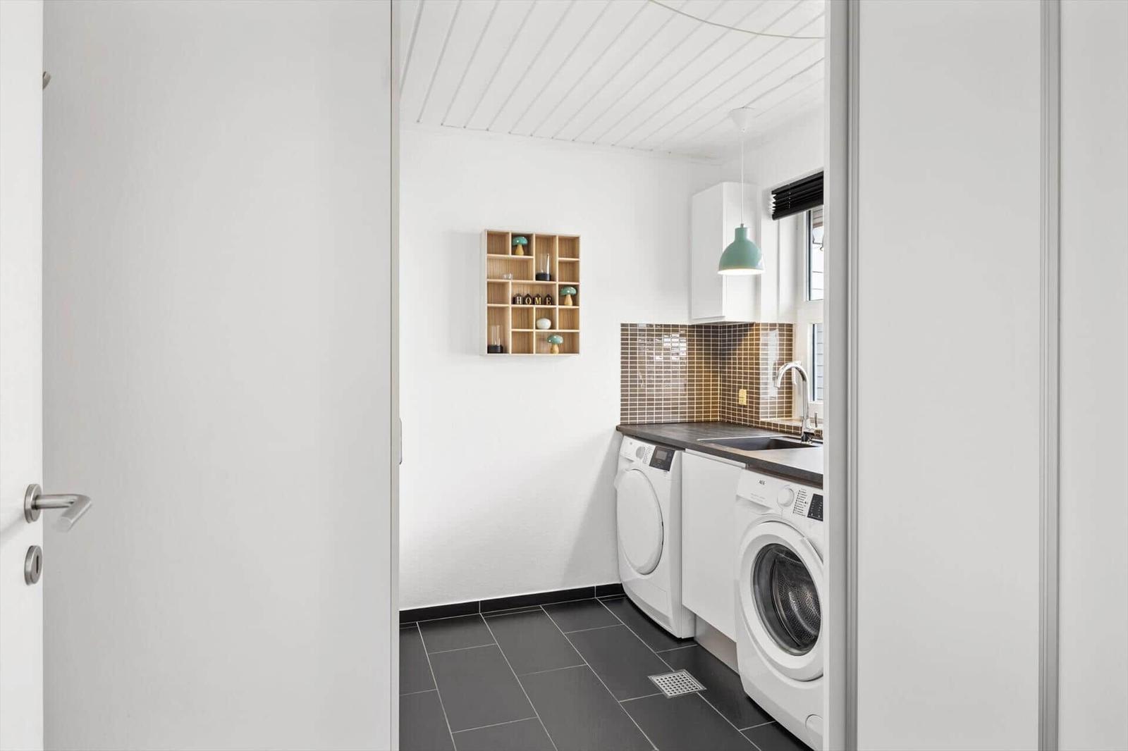 Waschraum mit Waschmaschine, Spüle und Holzregal an der Wand.
