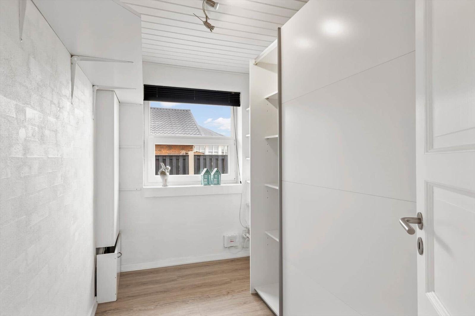 Schlafzimmer mit weißem Schrank und Fensterblick auf Dach