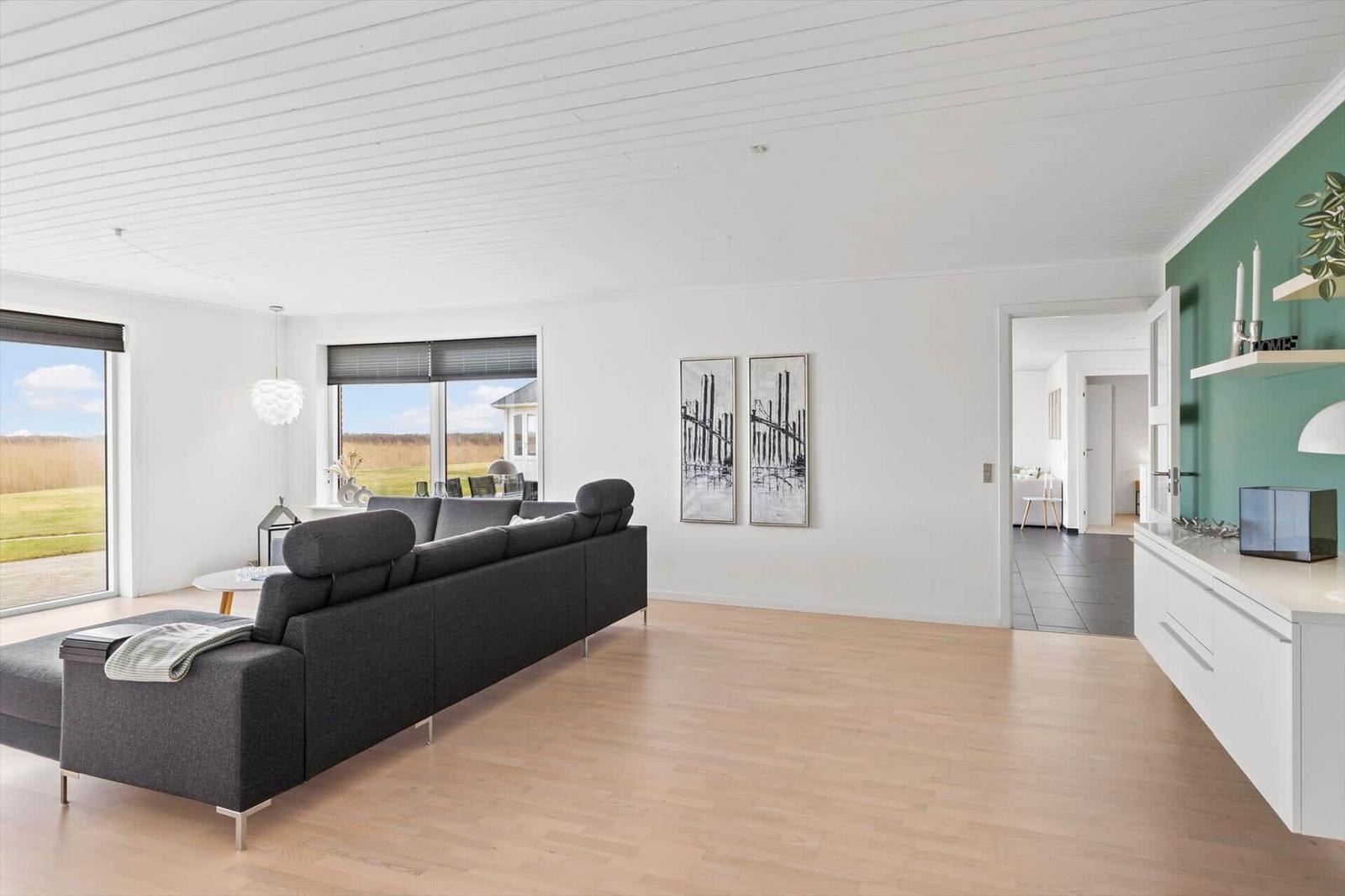 Wohnzimmer mit grauem Sofa, Holzboden und Blick auf das Feld.