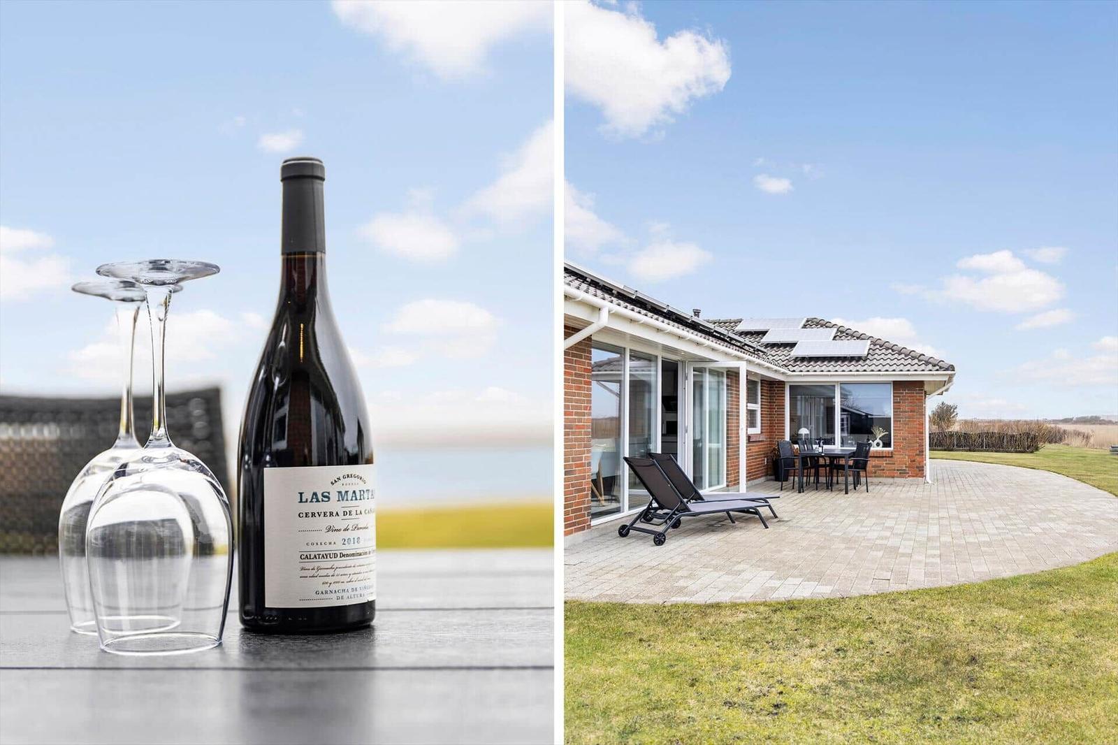 Wein und Gläser auf Tisch. Ferienhaus mit Terrasse, Liegestühlen und Garten.