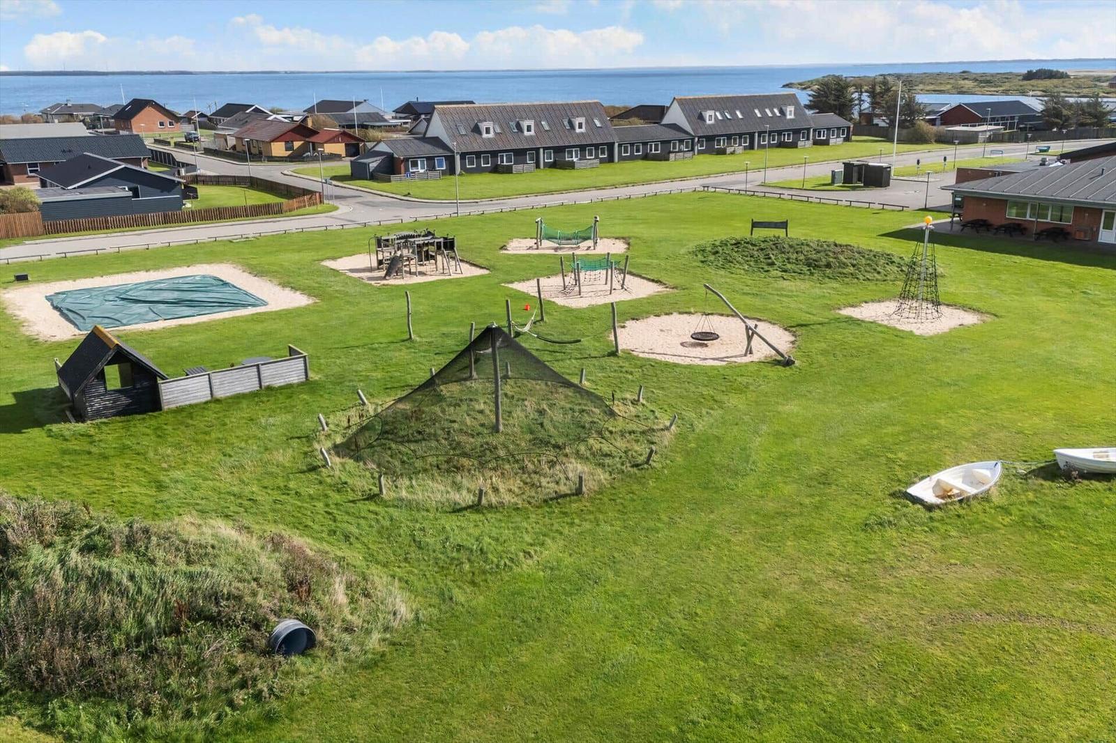Grüner Spielplatz mit Sandkästen, Klettergerüsten und Bootsanlegestelle am See
