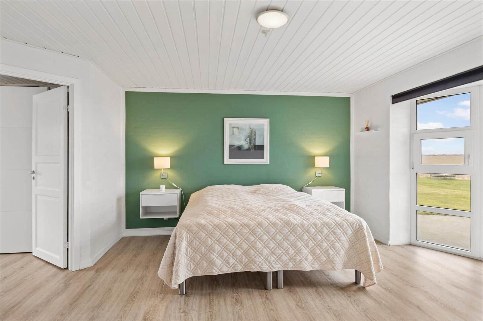 Schlafzimmer mit grüner Wand, Bett, Nachttischen und Fenster.