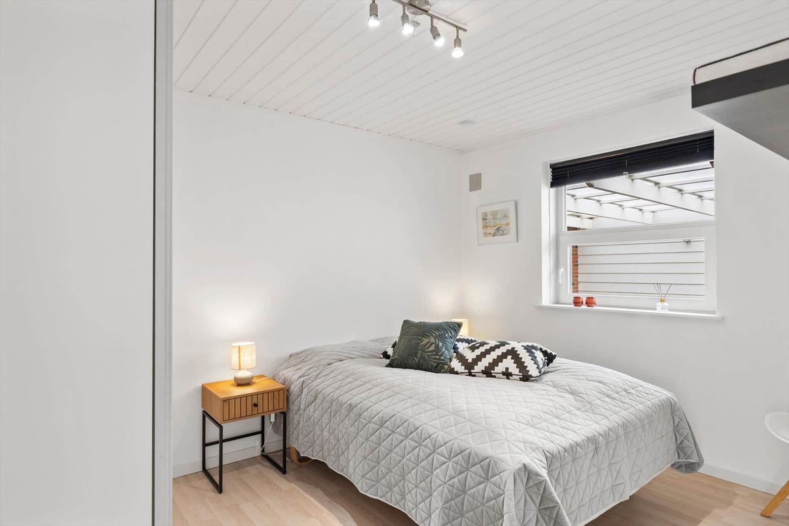 Schlafzimmer mit Bett, Nachttisch und Fenster mit Blick auf Terrasse.