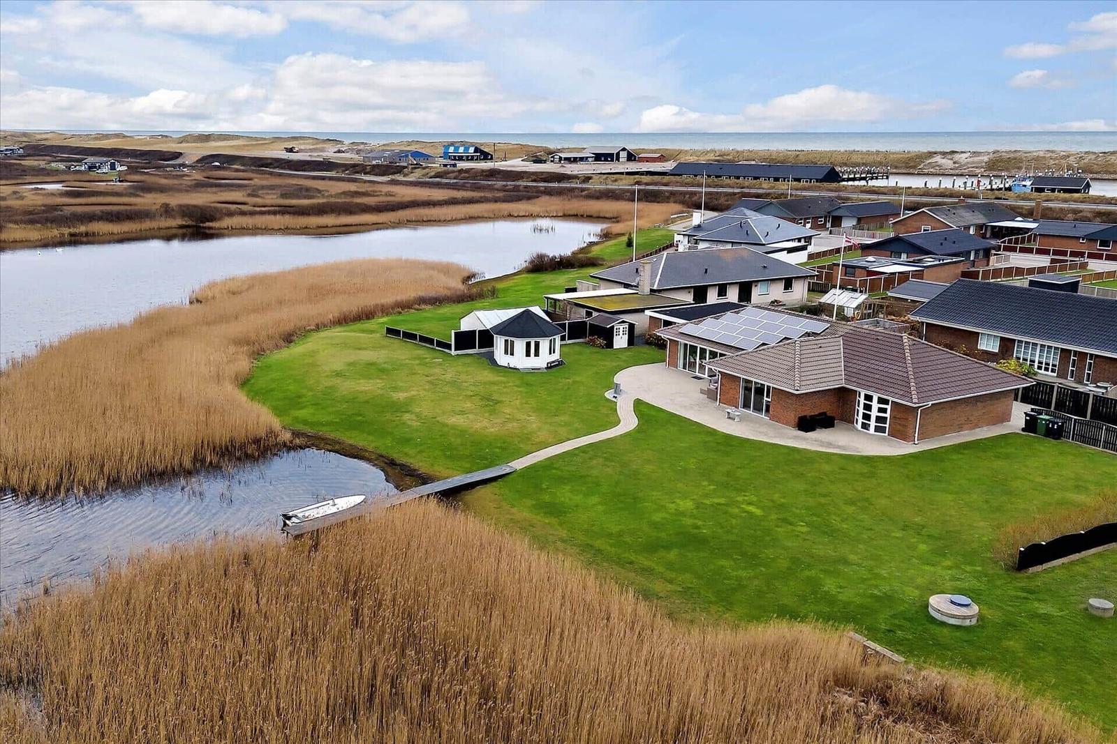 Haus mit Garten und Bootssteg am Wasser, Blick auf Strand und Himmel.
