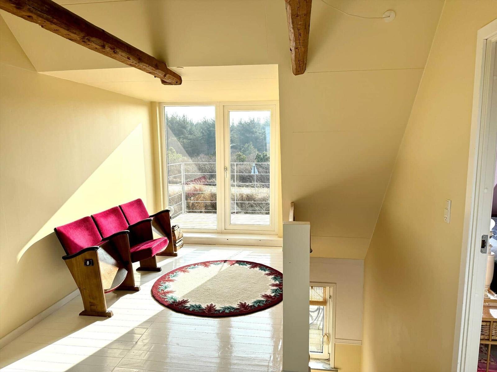 Raum mit rotem Sitzmöbel, runden Teppich und Fenster zur Terrasse.