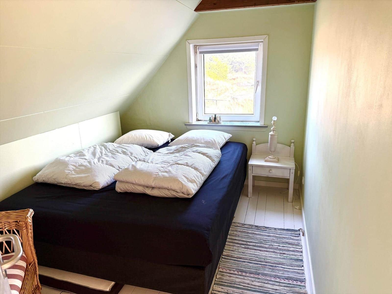 Schlafzimmer mit Doppelbett, Fenster und Nachttisch.
