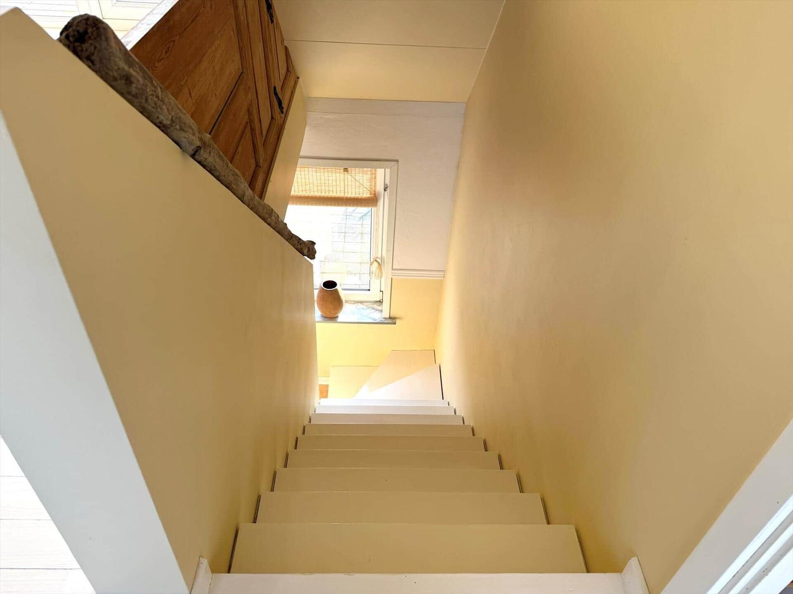 Helle Treppe mit Holzgeländer und Fenster im oberen Stockwerk.