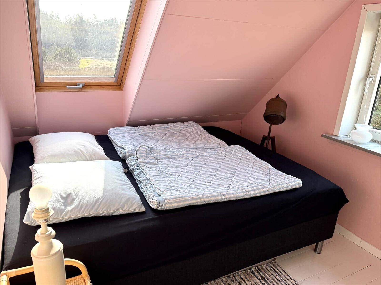 Schlafzimmer mit Dachschrägen, Bett, Fenster und Nachttisch.