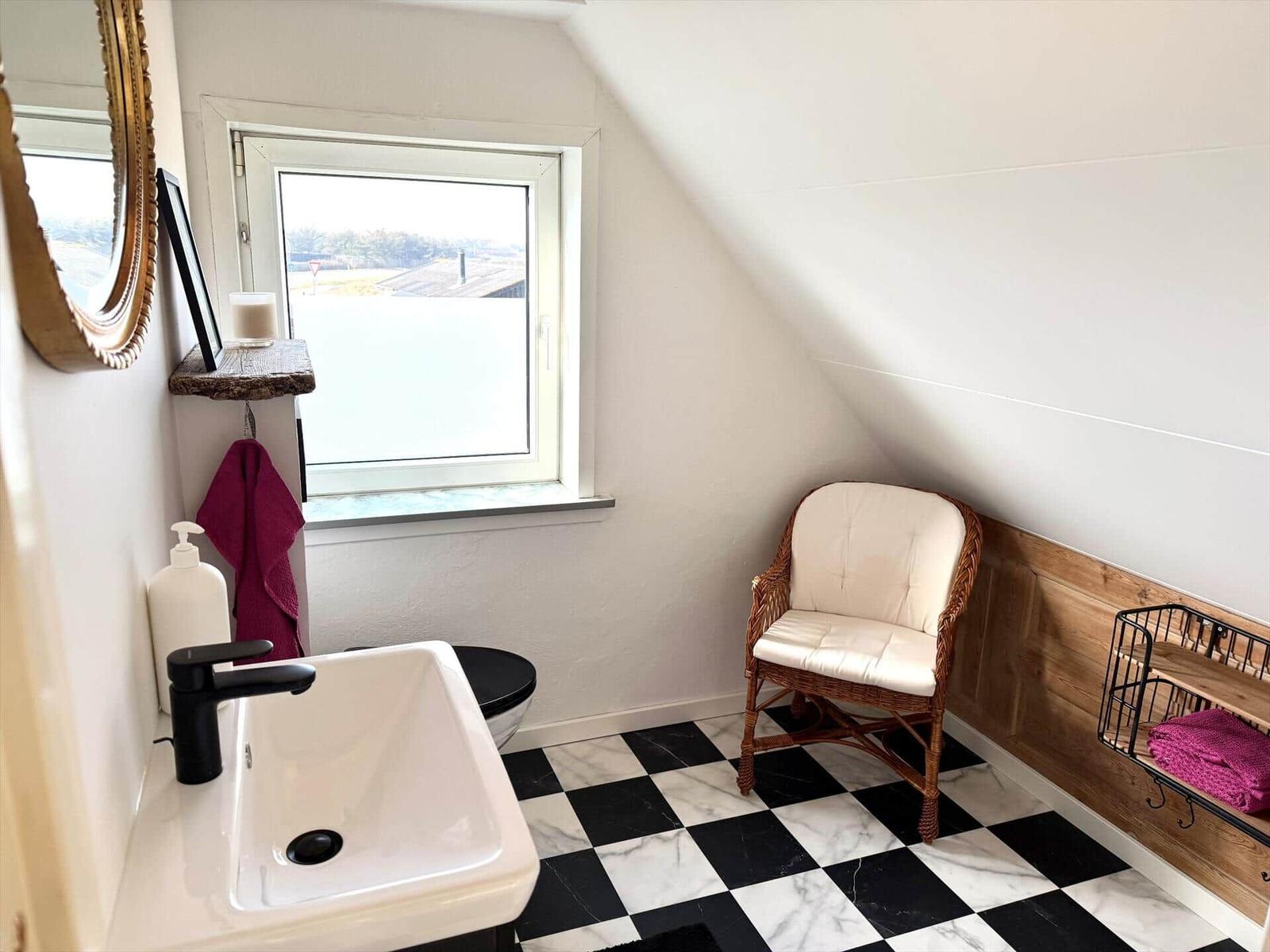 Badezimmer mit schwarz-weißem Fliesenboden, Waschbecken, Stuhl und Fenster.