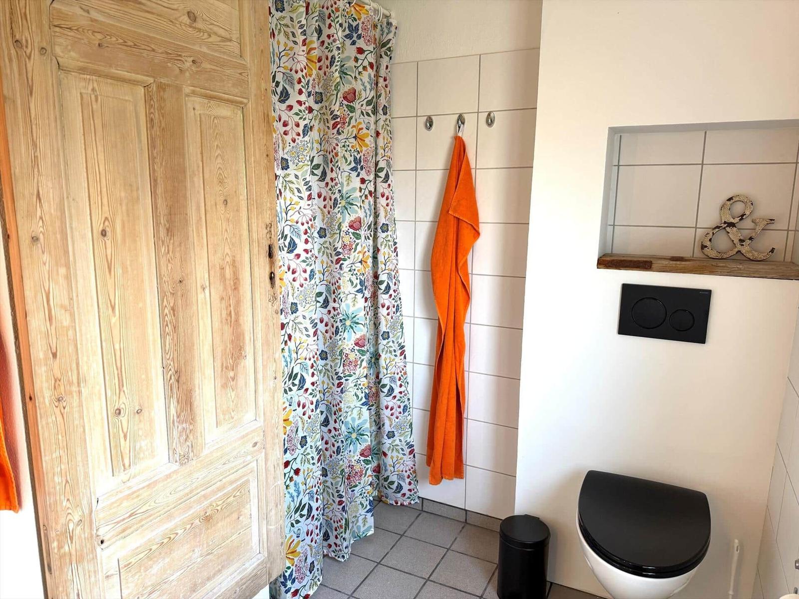 Bad mit Holztür, blumigem Duschvorhang und orangefarbenem Handtuch.