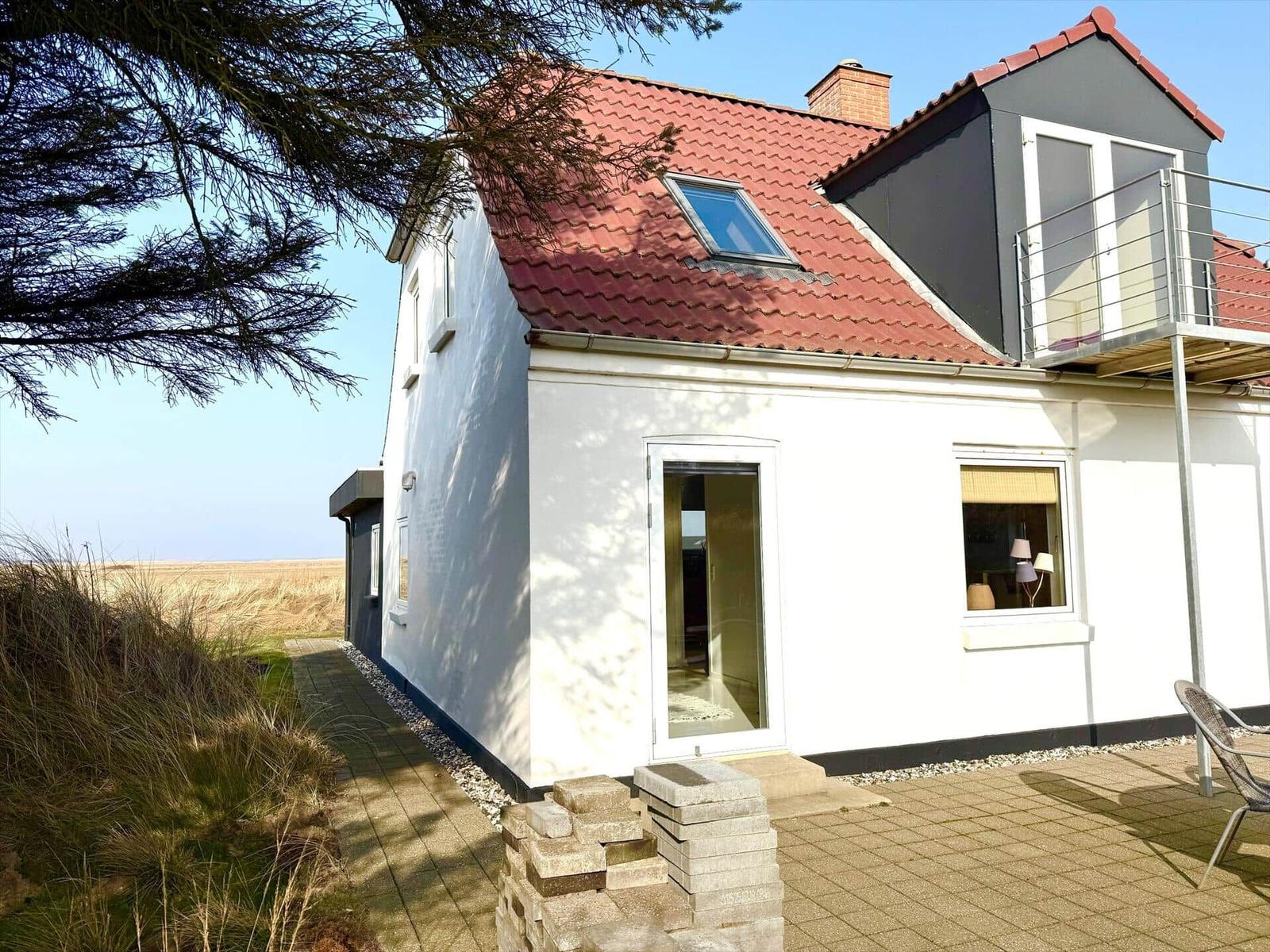 Wohnhaus mit rotem Dach, Terrasse und Balkon. Blick auf Felder und Himmel.