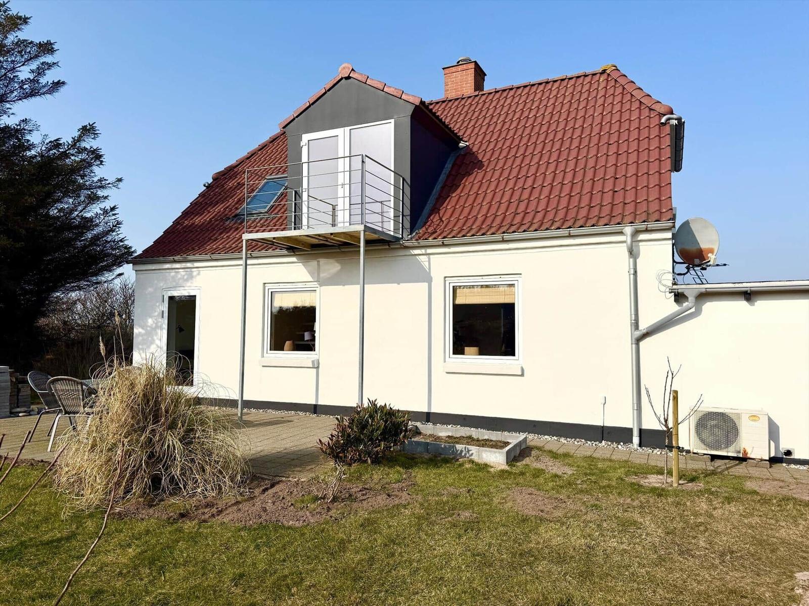 Ein Haus mit rotem Dach und weißer Fassade. Auf dem Dach befindet sich eine Terrasse mit Glasfronten.