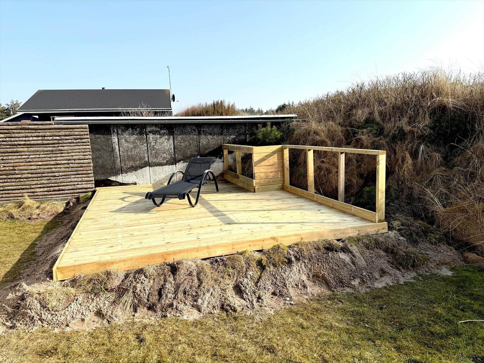 Holzterrasse mit Liegestuhl und Geländer im Freien.