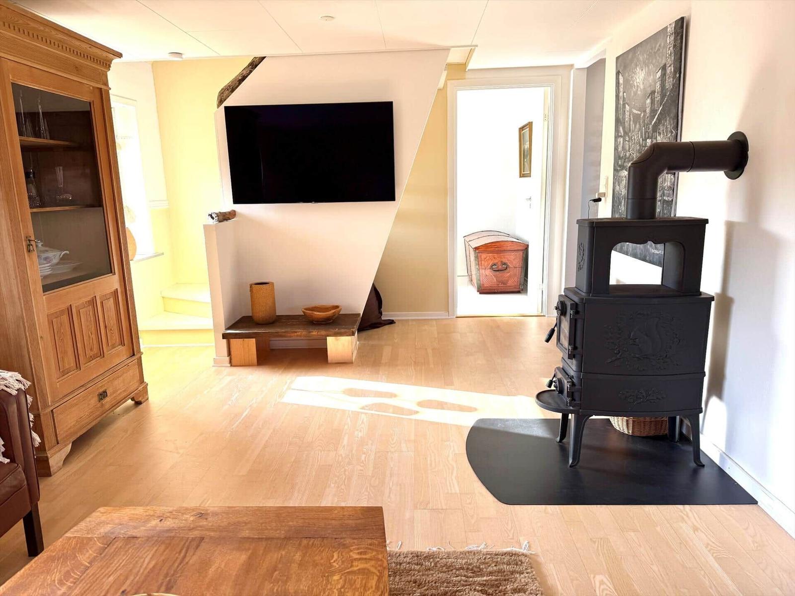 Wohnzimmer mit Holzboden, Kaminofen und Wandfernseher.
