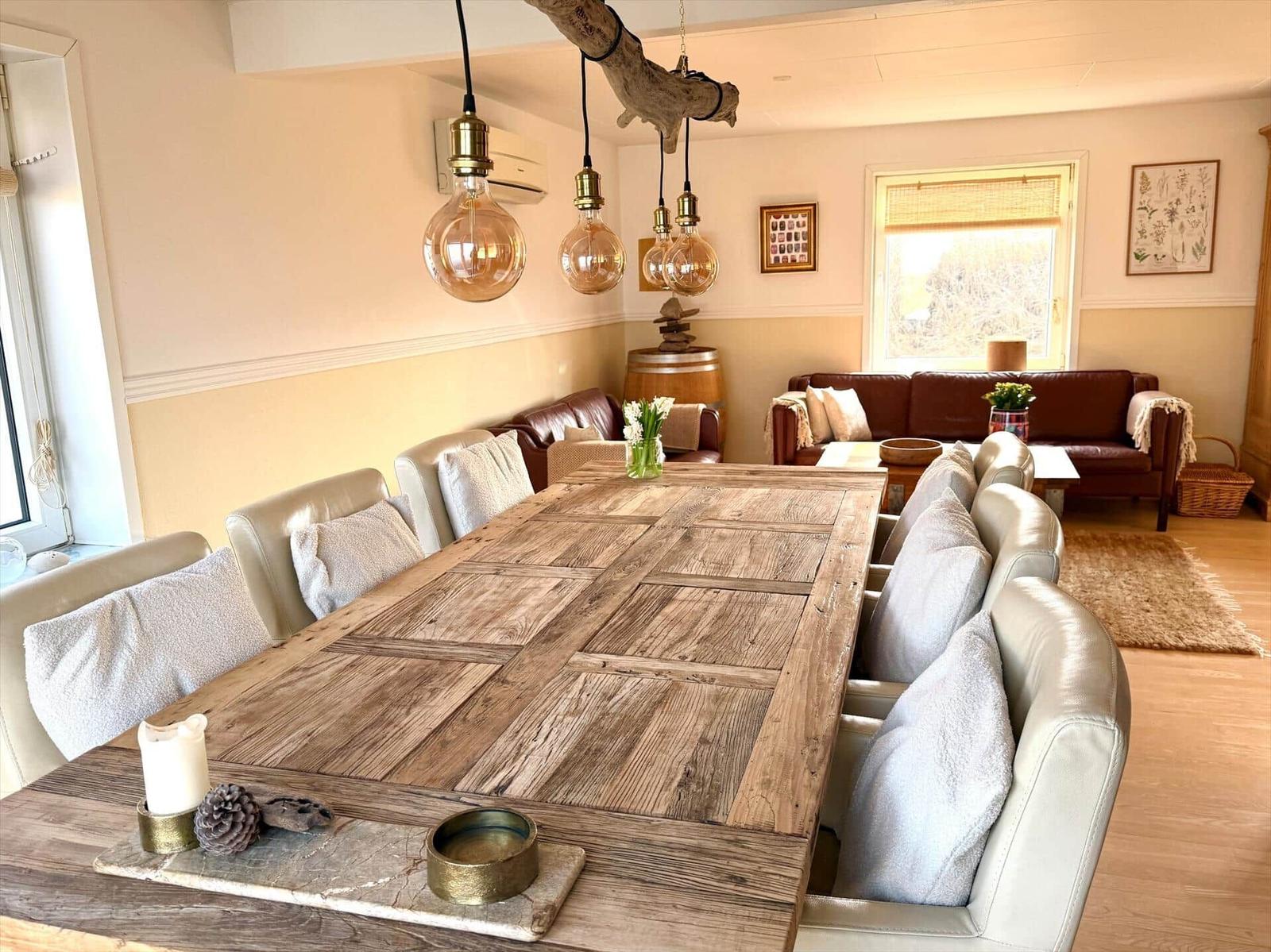 Großer Esstisch mit Lederstühlen und Holzdecke. Hängelampen und Sofa im Hintergrund.