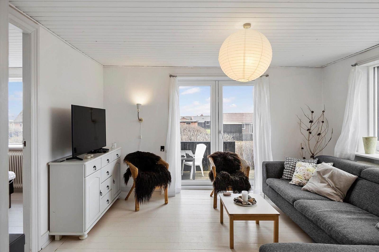 Wohnzimmer mit Sofa, Fernseher und Blick auf Balkon