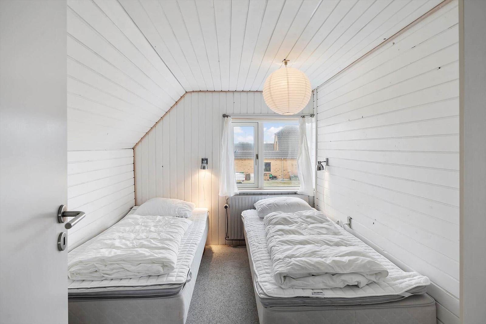 Zwei Betten in einem schrägen Dachzimmer mit Fenster und Lampe.