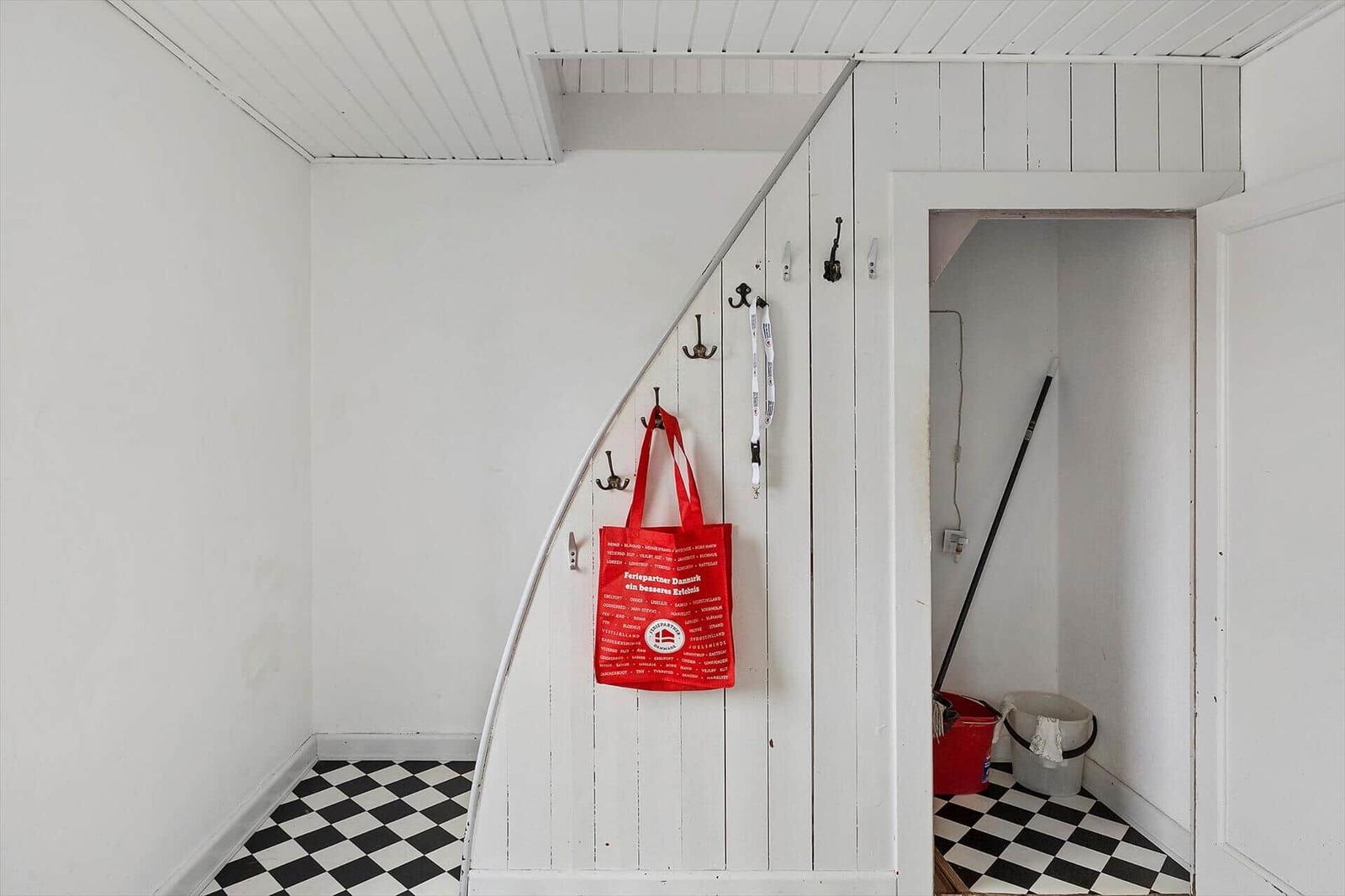Eingangsbereich mit schwarz-weißem Fliesenboden und roter Tasche an der Wand.