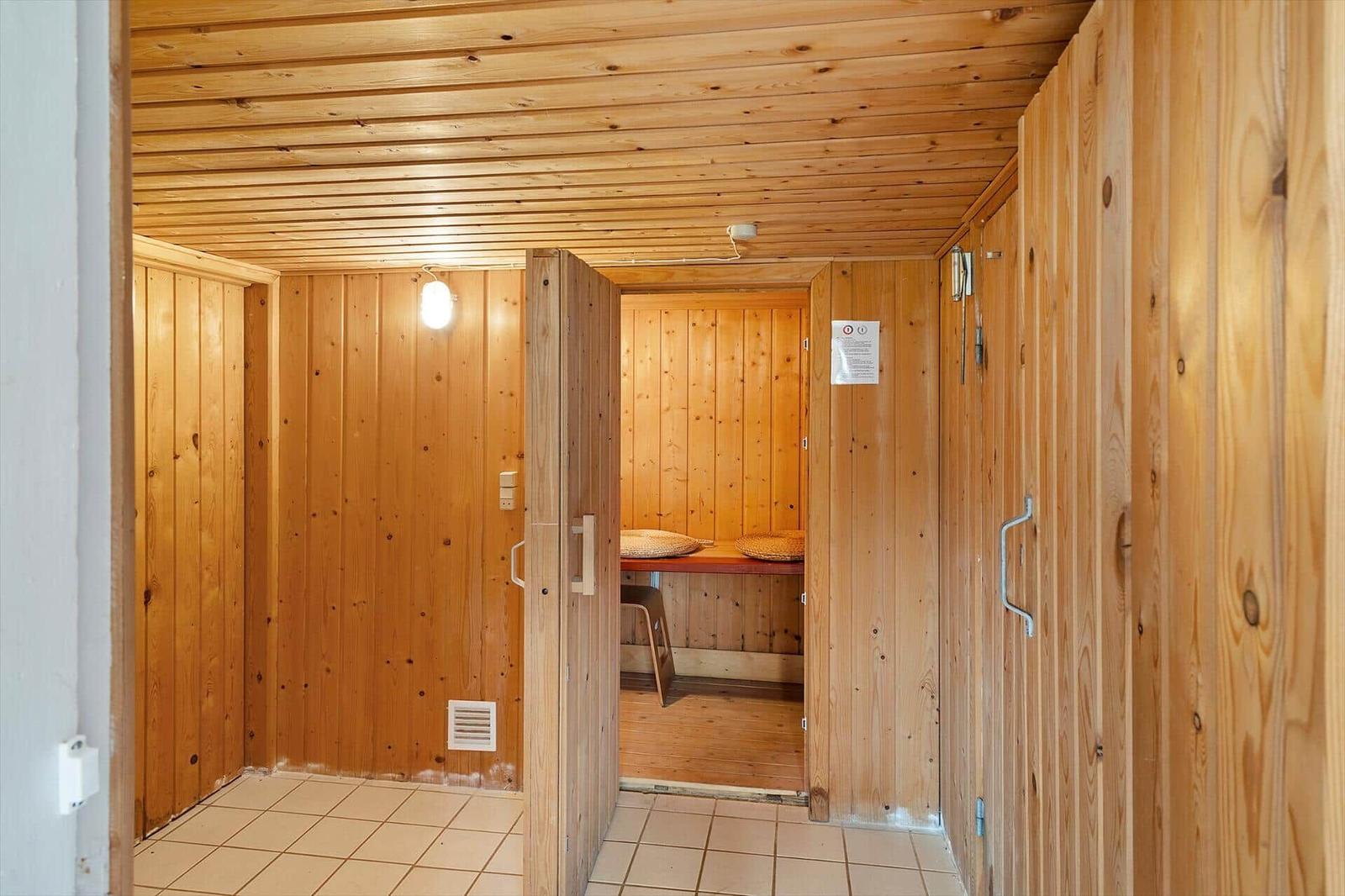 Holzsauna mit Sitzbänken und Tür. Fliesenboden und Holzwände.